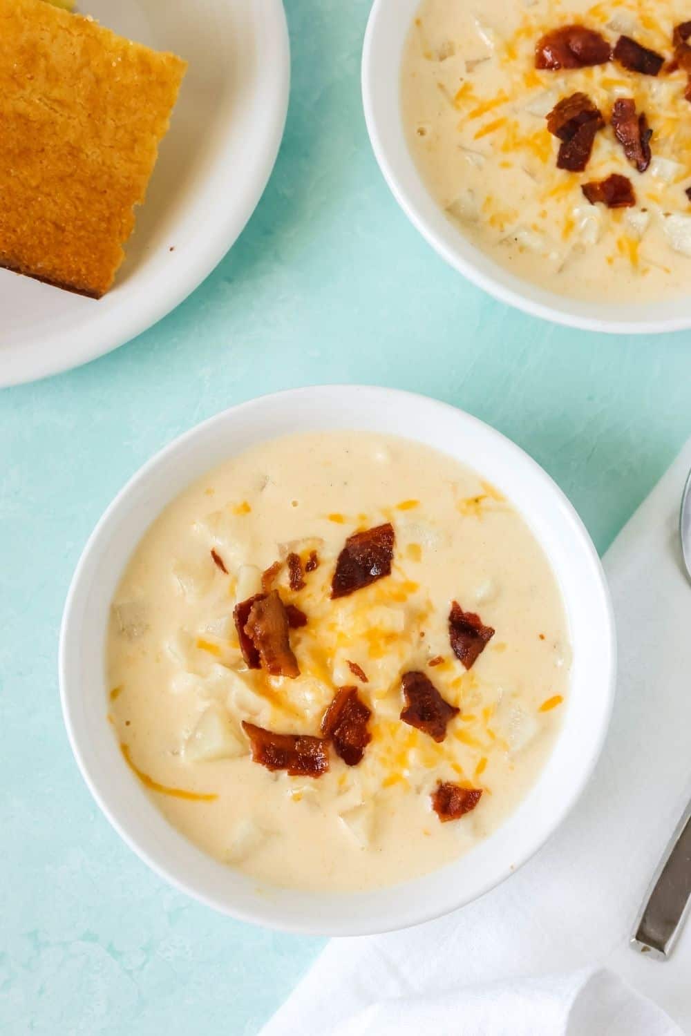 overhead view of two white bowls of hash brown cheesy potato soup and a plate of cornbread.