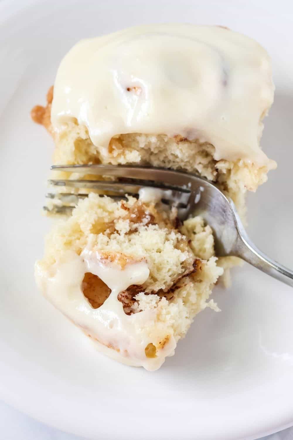 close-up view of a Bisquick cinnamon roll on a white plate. A fork has cut into the roll, showing the moist interior and the brown sugar cinnamon filling.