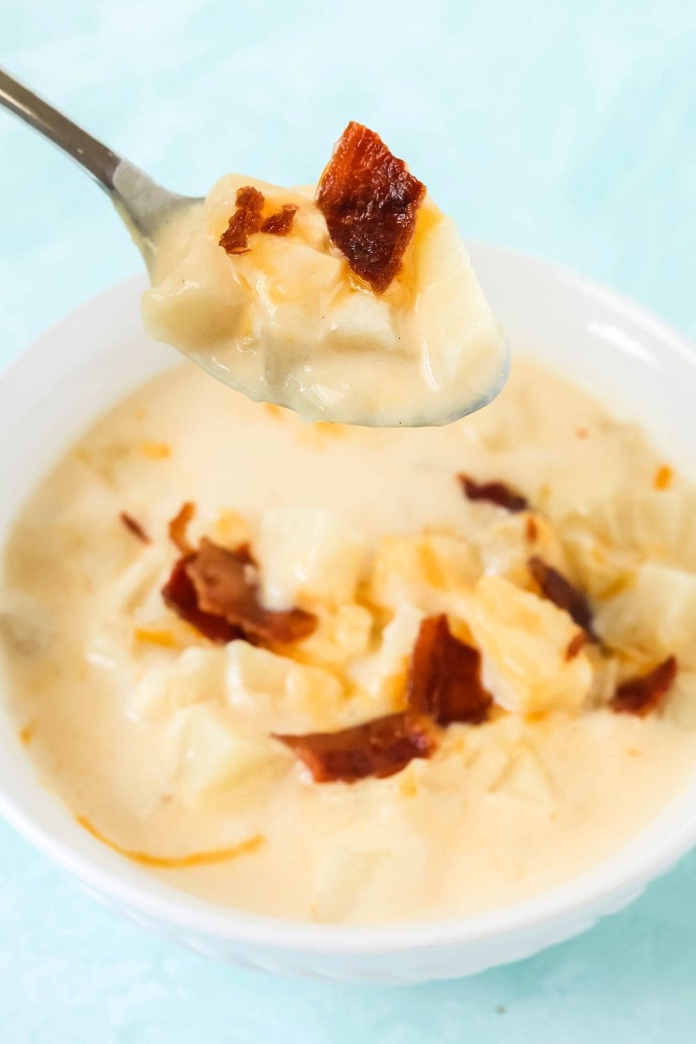close-up view of a spoon lifting a bite of hash brown potato soup out of a white bowl.