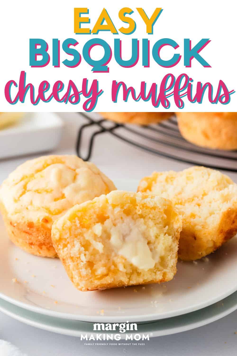 close-up view of twp Bisquick cheesy muffins, one of which is halved and smeared with softened butter, served on a white plate.