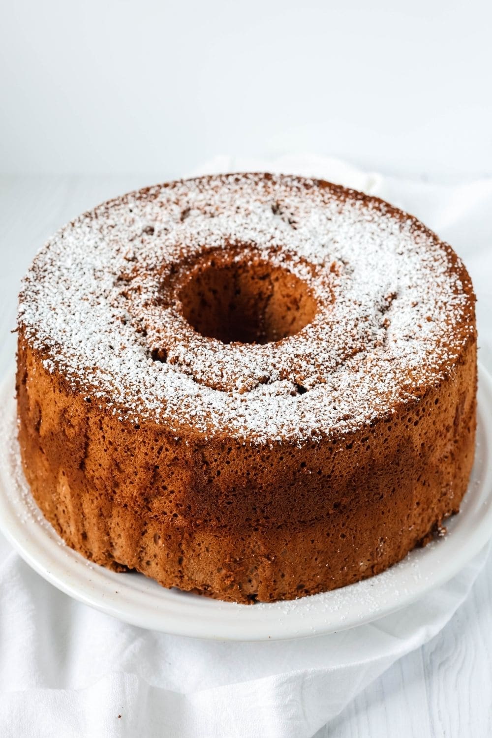 a chocolate angel food cake is served on a white plate, dusted with powdered sugar on top.