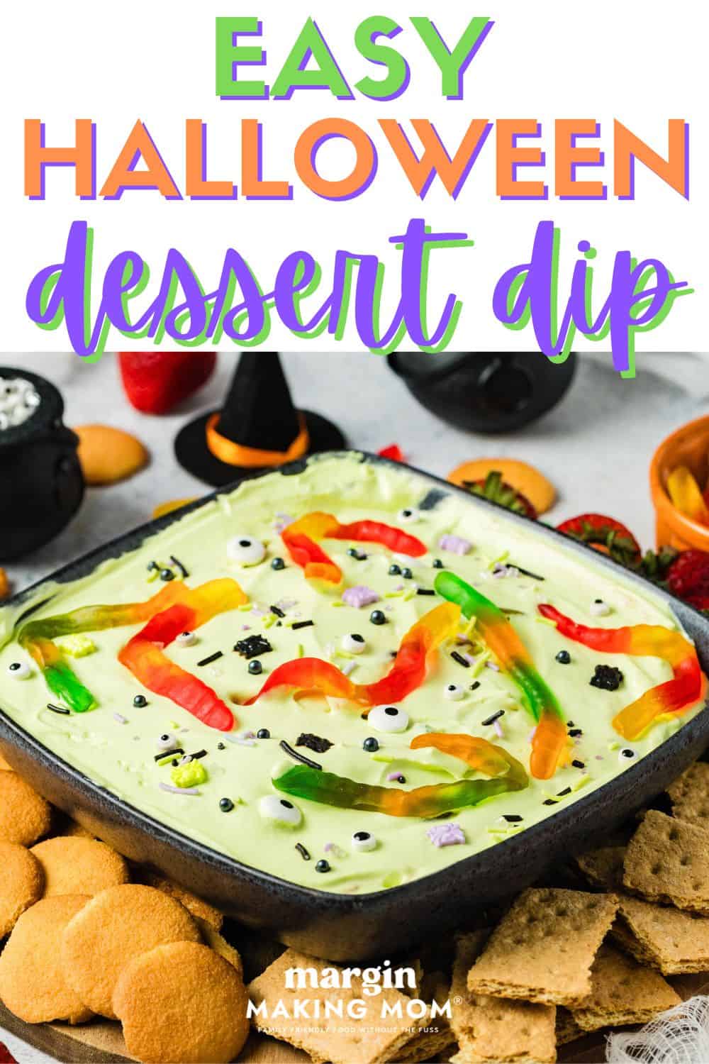 a black bowl of Halloween dessert dip served alongside fresh fruit, vanilla wafers, and graham crackers.