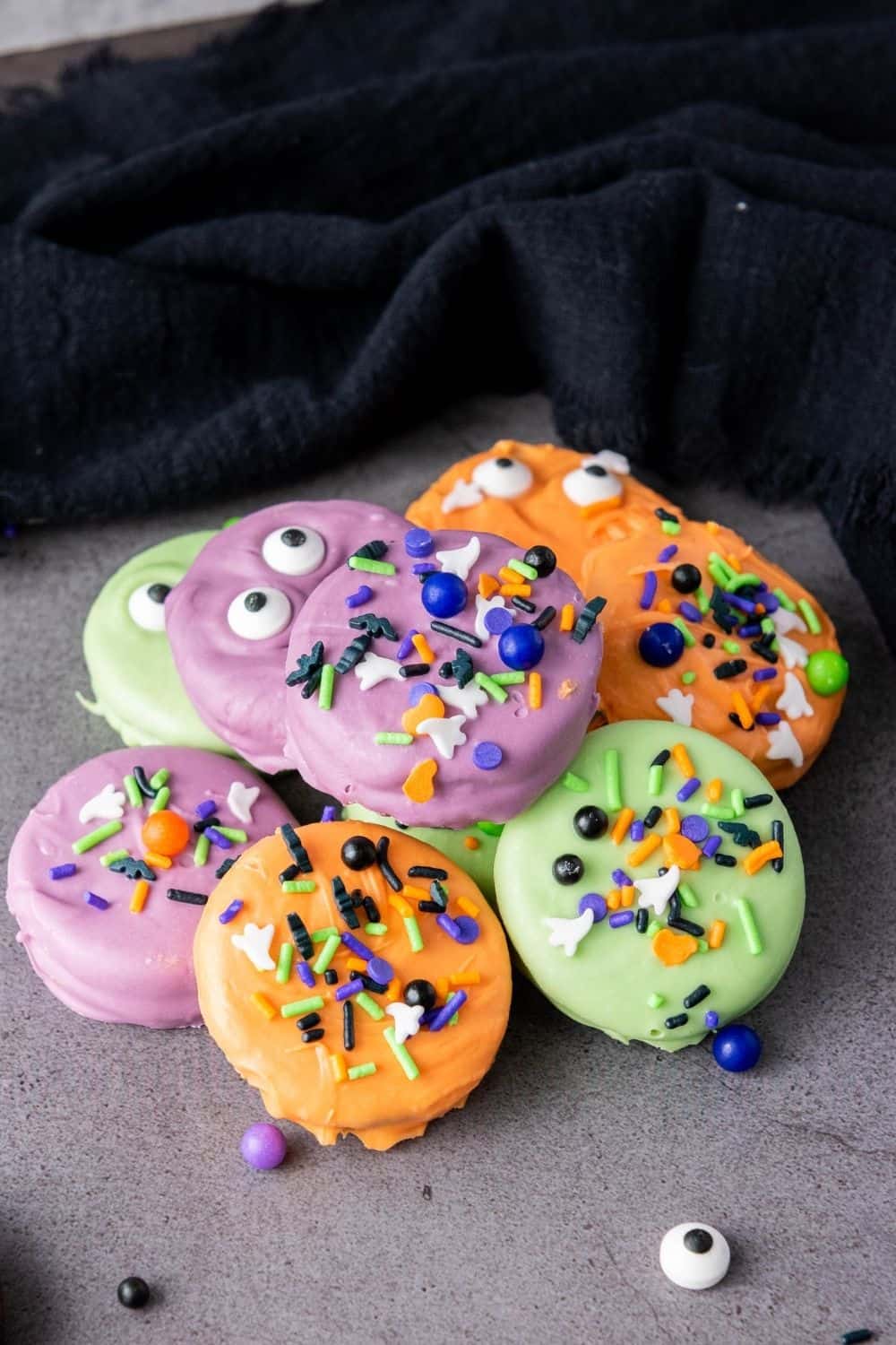 Several Oreos decorated for Halloween by being dipped in orange, purple, or green candy melts, then decorated with sprinkles.