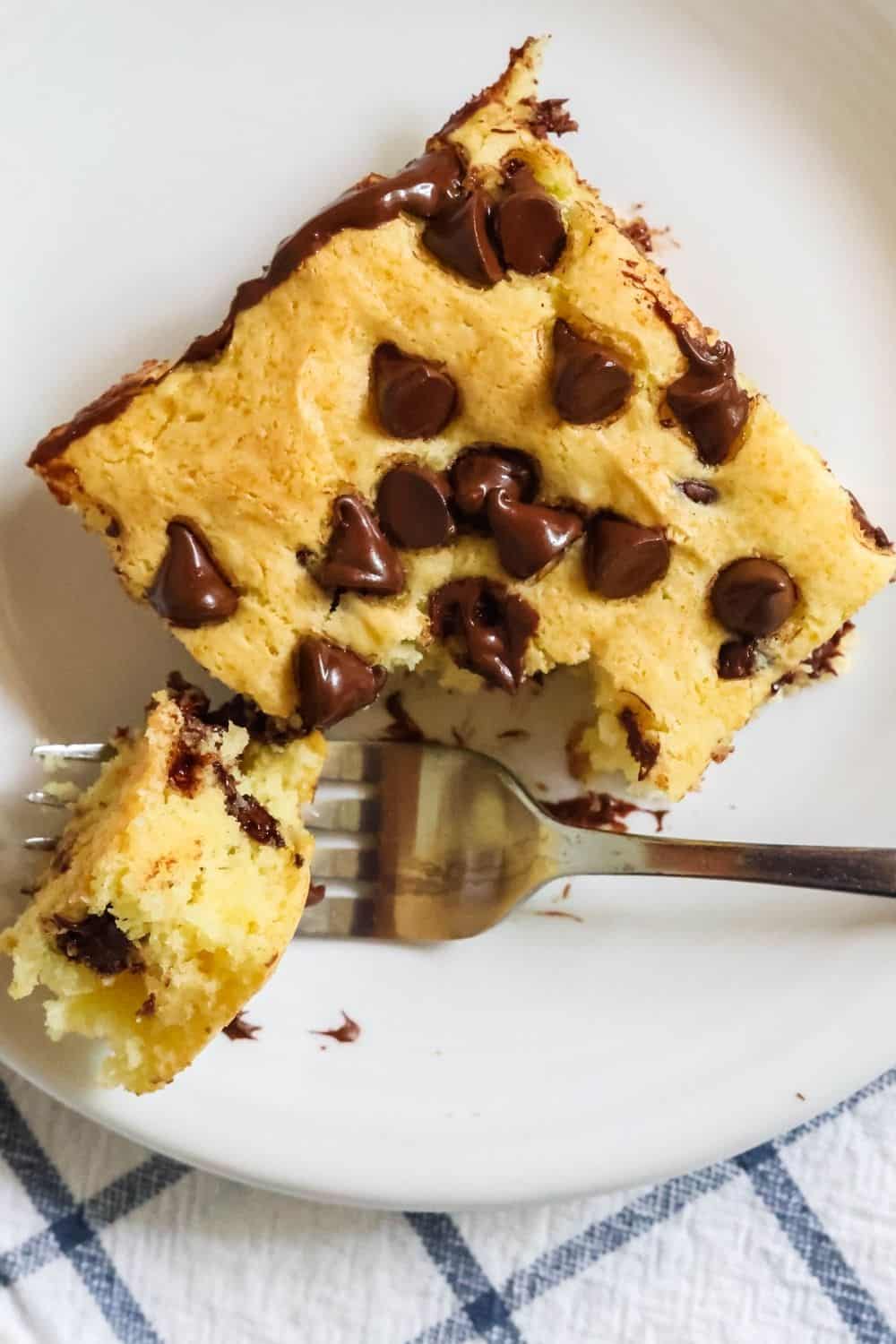 overhead view of a square of vanilla pudding cake made with chocolate chips. A fork has cute a bite out of the square.