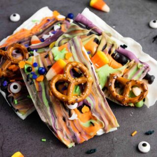 Halloween bark pieces, decorated with pretzels, candy corn, and Halloween sprinkles, displayed on a black surface.