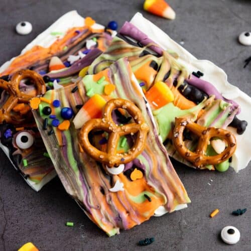 Halloween bark pieces, decorated with pretzels, candy corn, and Halloween sprinkles, displayed on a black surface.