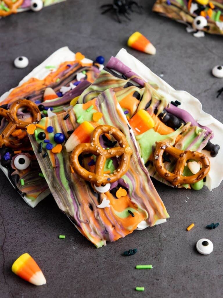 Halloween bark pieces, decorated with pretzels, candy corn, and Halloween sprinkles, displayed on a black surface.