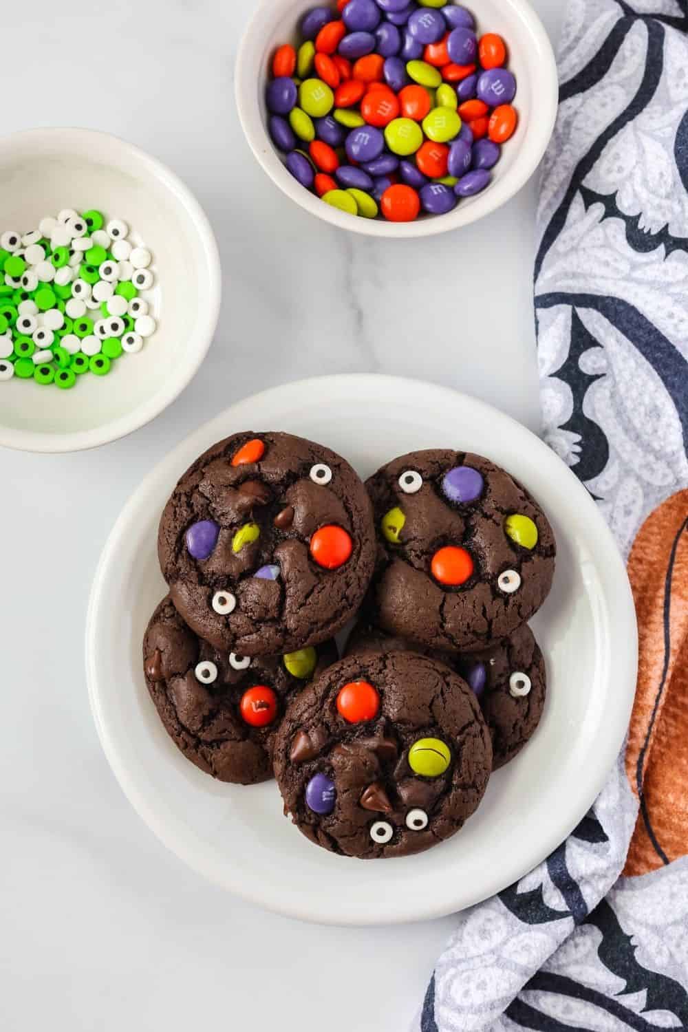overhead view of cake mix Halloween cookies served on a white plate, with two small bowls of candy eyeballs and Halloween M&Ms next to the plate.