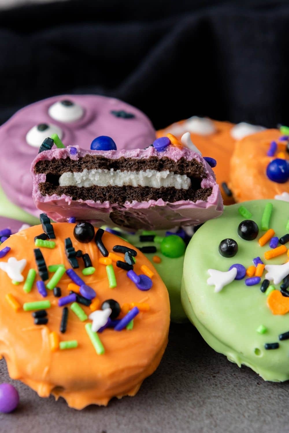 close-up of Halloween themed Oreos decorated with sprinkles. One Oreo has a bite taken out of it.