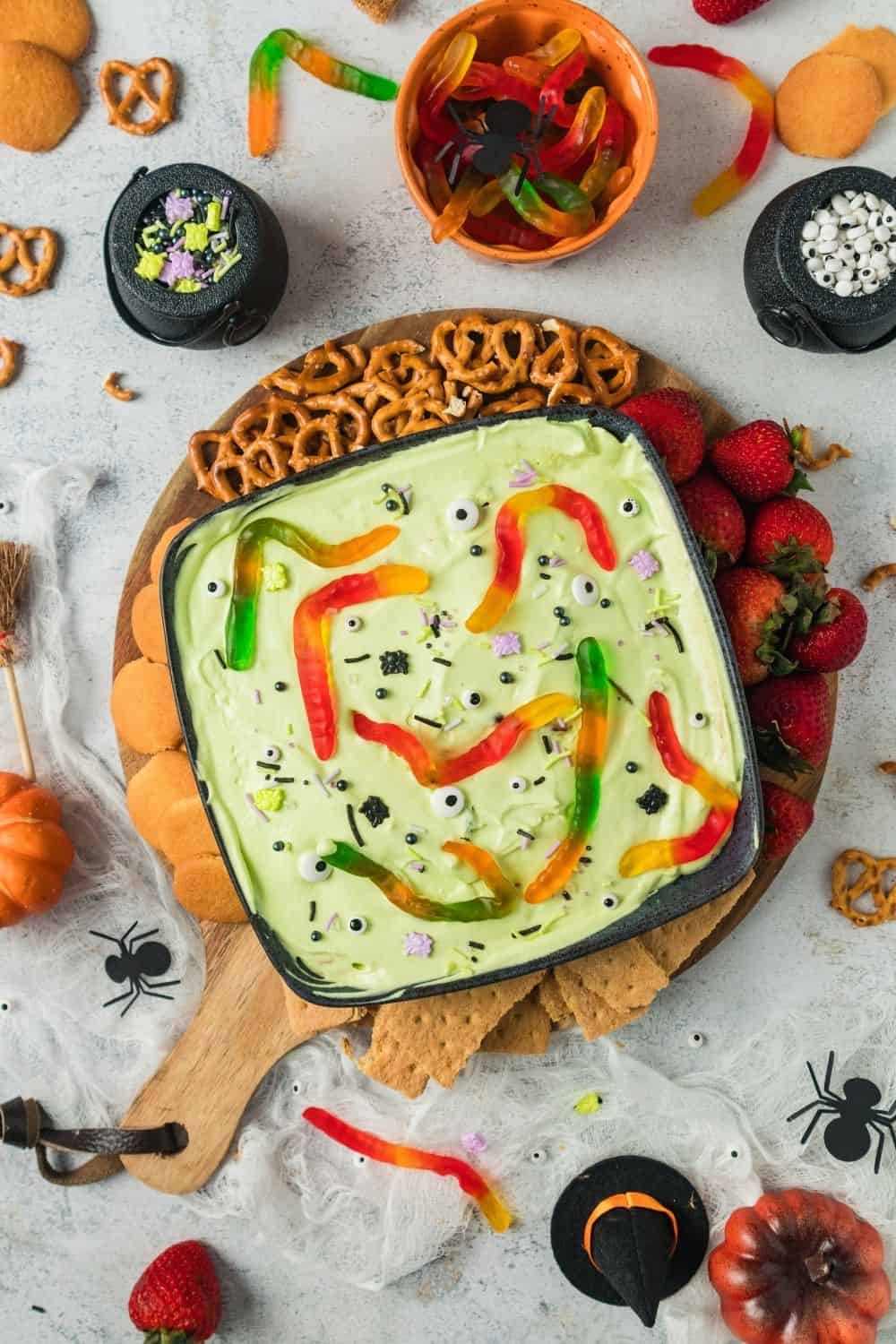 no bake dessert dip for Halloween, served in a black bowl and surrounded with various dippers, such as pretzels, berries, cookies, and graham crackers.