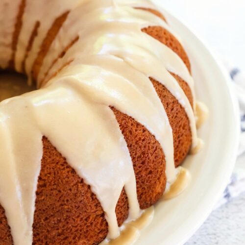 A peach bundt cake from a mix is topped with brown sugar icing and served on a white plate.