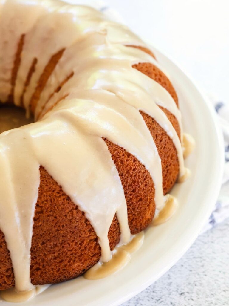 A peach bundt cake from a mix is topped with brown sugar icing and served on a white plate.