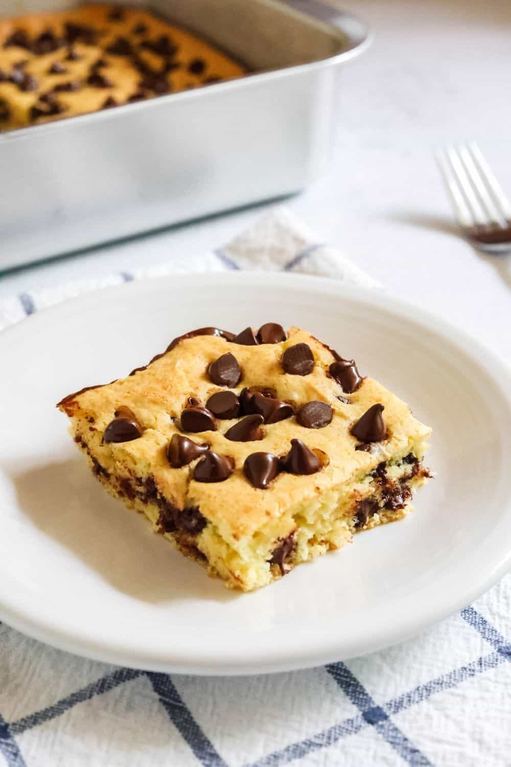 a square slice of vanilla and chocolate chip cake bars is served on a white plate.
