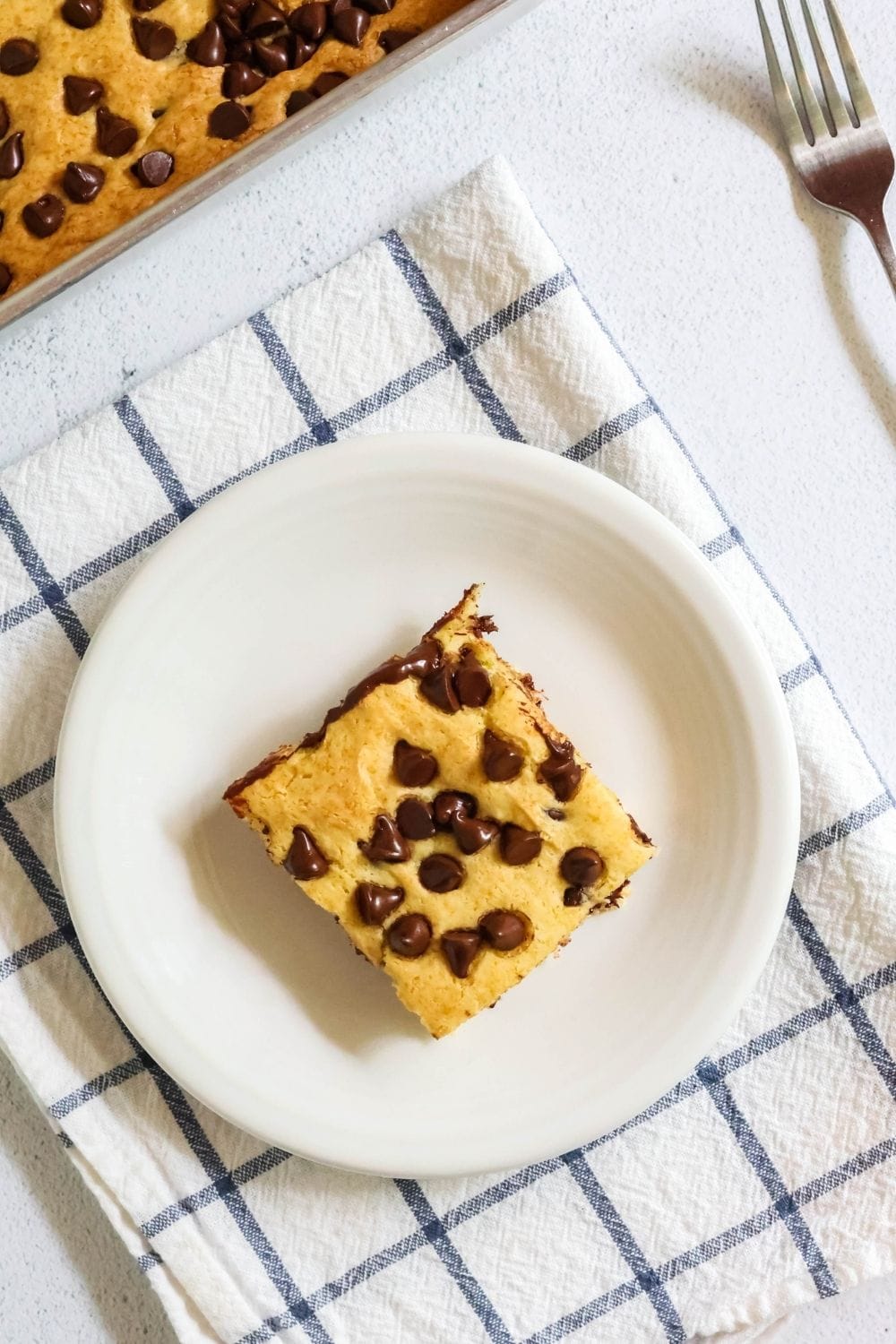 overhead view of a slice of vanilla pudding dump cake, dotted with melty chocolate chips, served on a white plate.