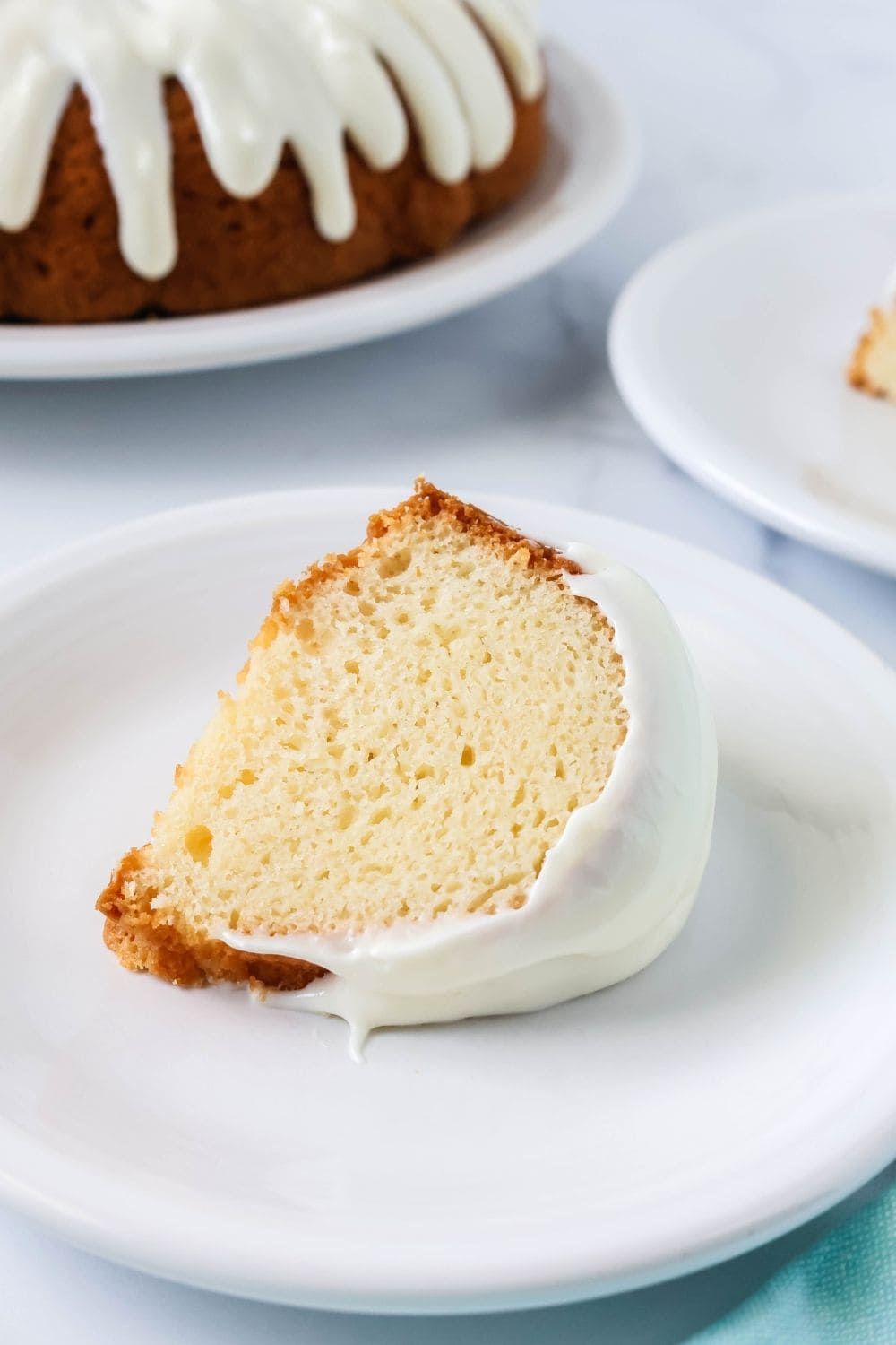slice of southern white pudding cake made with mayonnaise, served on a white plate with a bundt cake in the background.