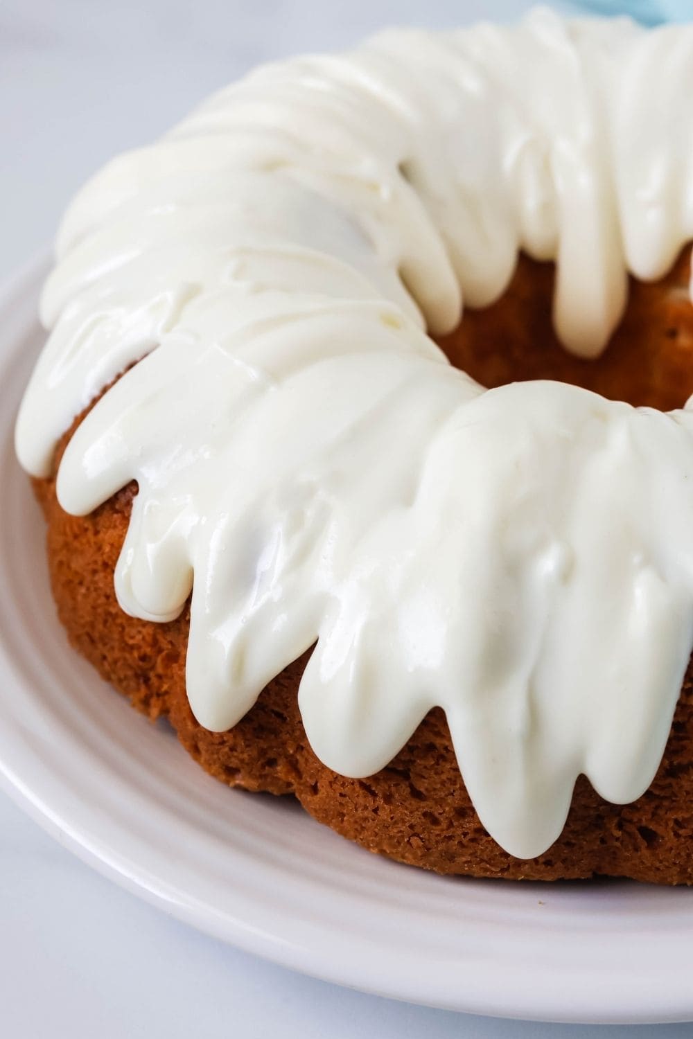close-up side view of a white pudding cake made with a mix. It's a bundt cake on a white plate, and the cake is topped with cream cheese icing.