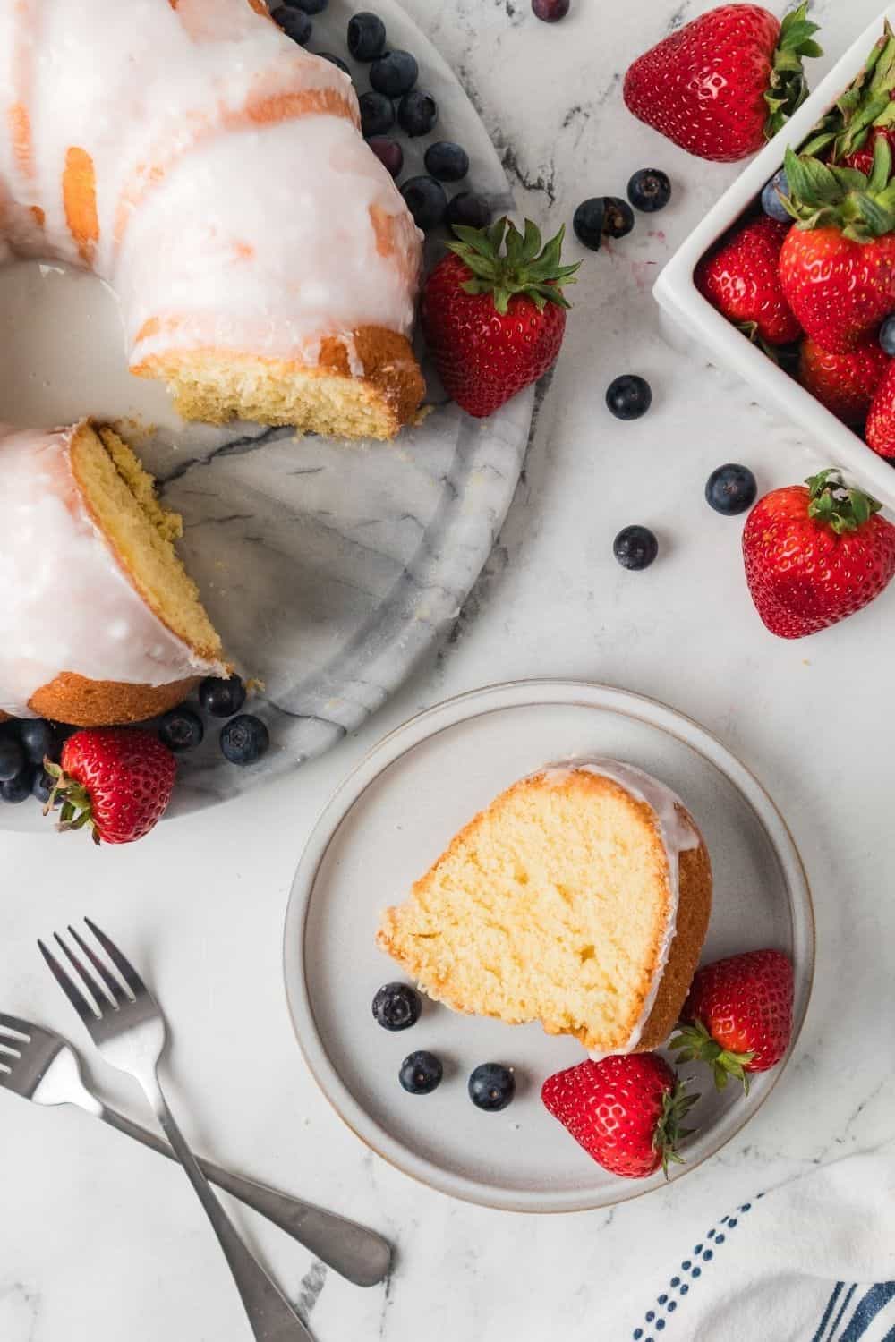 overhead view of a slice of pudding pound cake on a white plate, with the remainder of the cake next to it. Fresh berries are scattered around.
