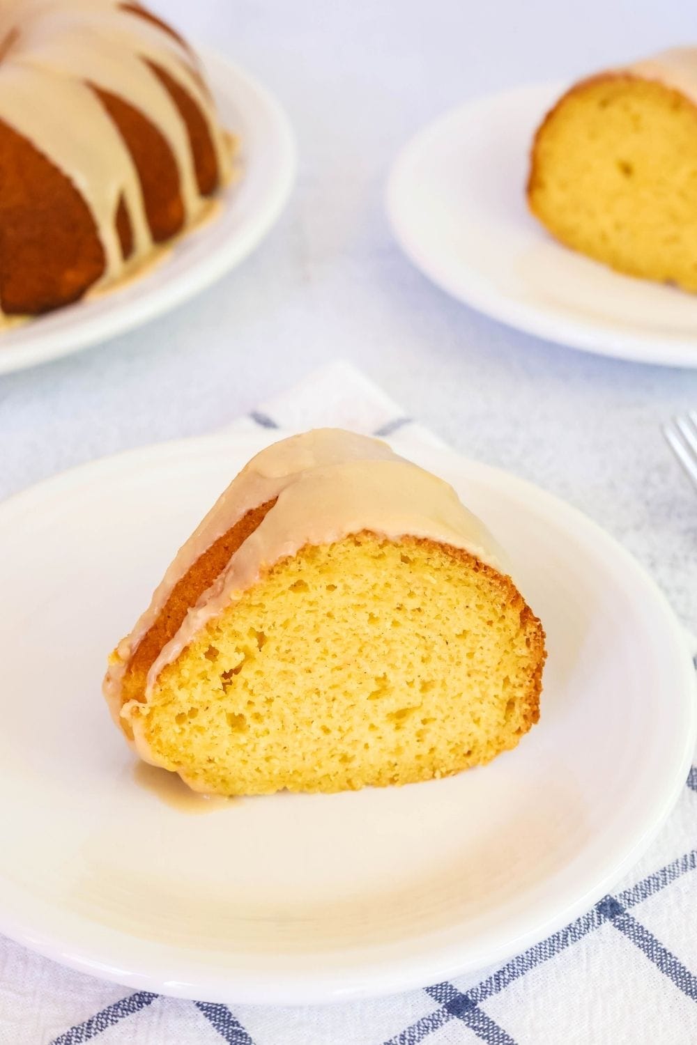 a slice of peach bundt cake on a white plate, with another slice and the whole cake in the background.