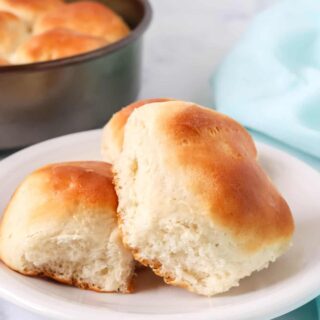 two Bisquick dinner rolls served on a white plate, with the pan of remaining yeast rolls in the background.