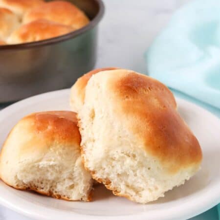 two Bisquick dinner rolls served on a white plate, with the pan of remaining yeast rolls in the background.