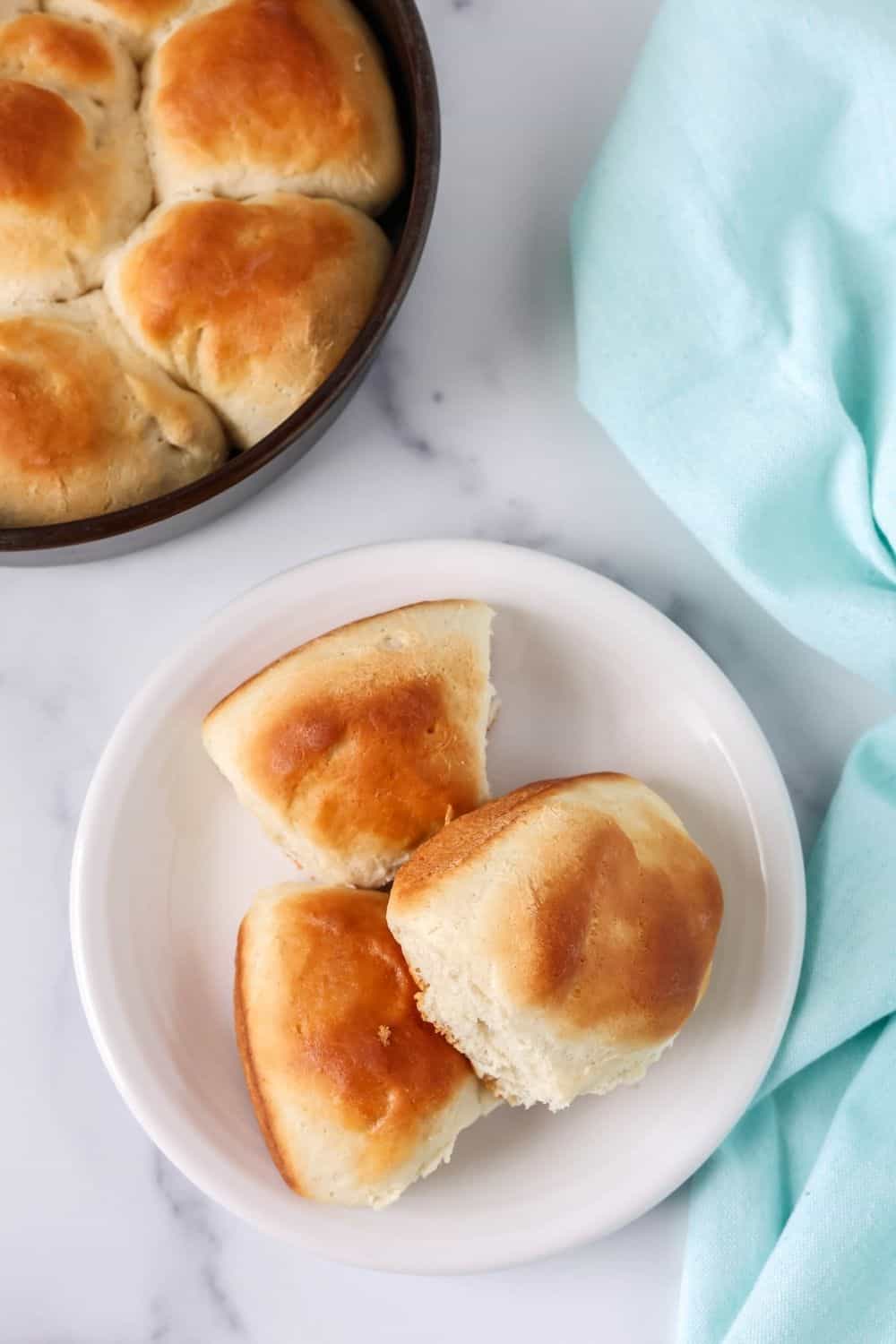 overhead view of three Bisquick rolls served on a white plate, with a pan of rolls in the background.