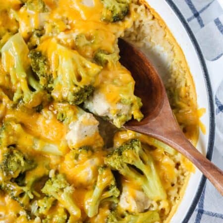 Cheesy chicken broccoli rice casserole in a Dutch oven pan. A wooden spoon is scooping out a serving of the casserole from the pan.