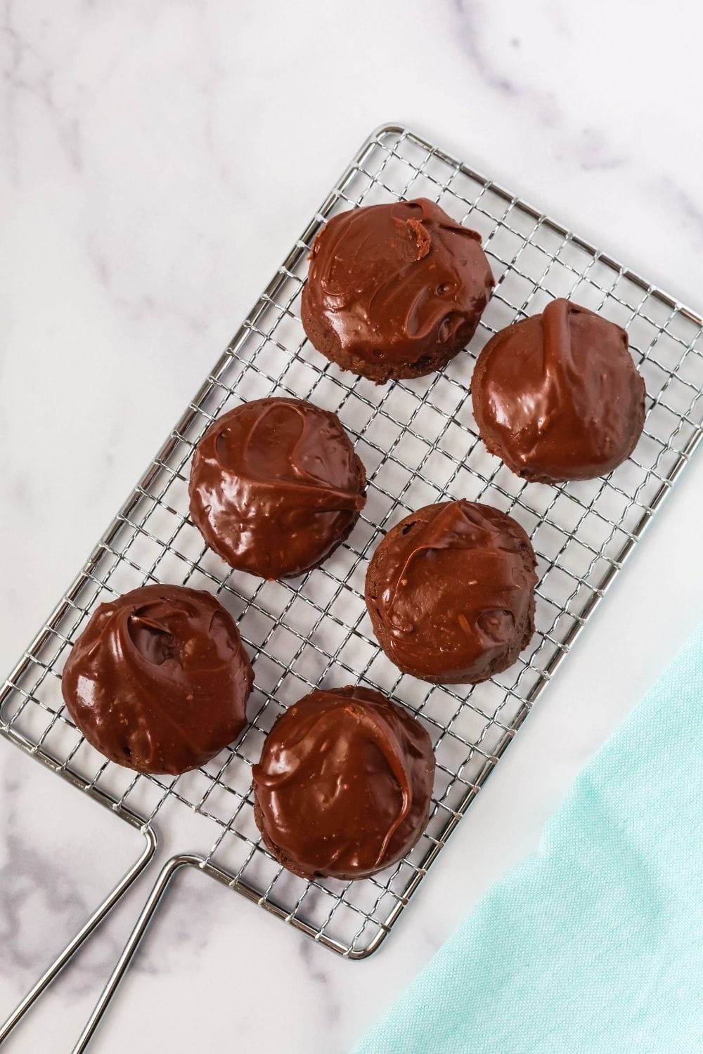 overhead view of six decadent chocolate cookies with icing that hardens, displayed on a wire rack.