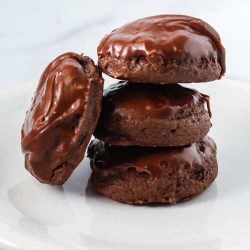 four chocolate cream cheese cookies with icing served on a white plate. Three cookies are stacked, while the fourth is leaned against the stack.