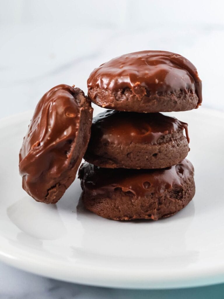 four chocolate cream cheese cookies with icing served on a white plate. Three cookies are stacked, while the fourth is leaned against the stack.