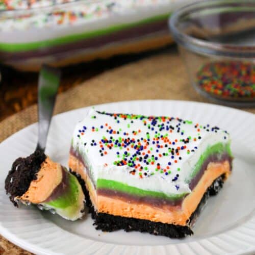 a slice of no-bake Halloween lush dessert served on a white plate. A fork has cute out a bite of the dessert.