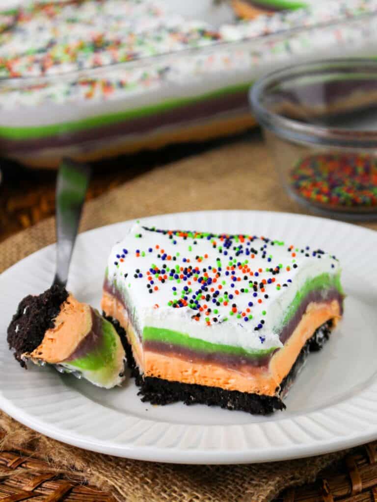 a slice of no-bake Halloween lush dessert served on a white plate. A fork has cute out a bite of the dessert.