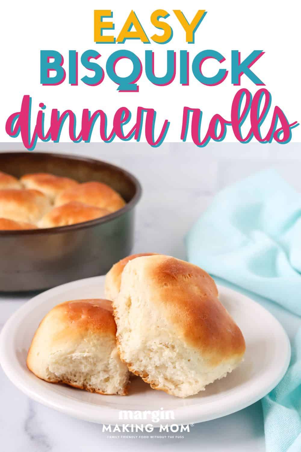 two Bisquick dinner rolls served on a white plate, with a cake pan of remaining dinner rolls in the background.