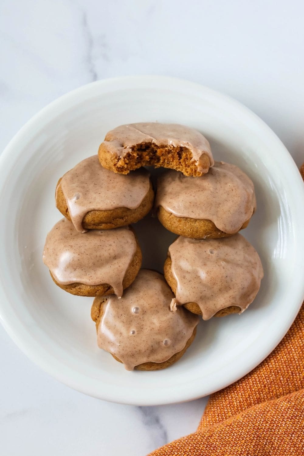 a white plate with six cake mix pumpkin cookies on it, each topped with icing. One of the cookies has a bite taken out of it.