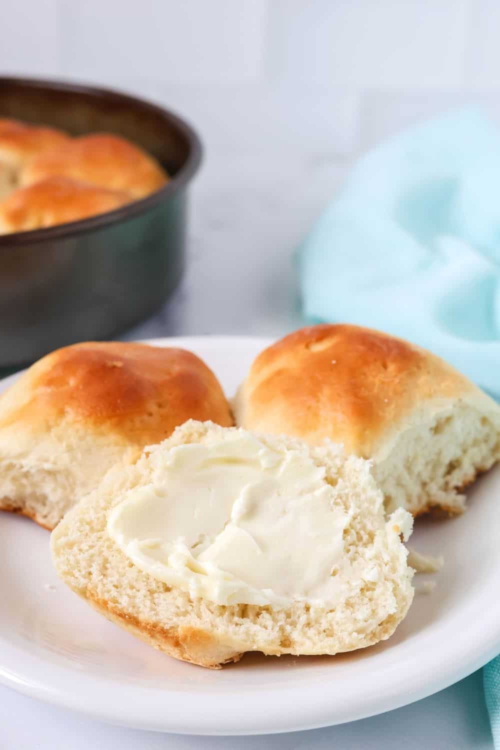 close-up view of Bisquick yeast rolls on a plate; one has been split open and spread with soft butter.