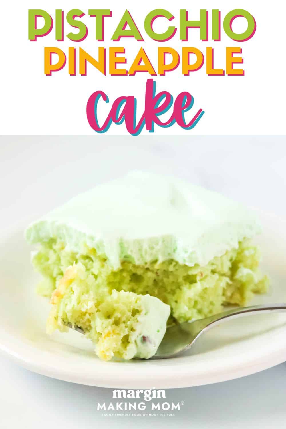 a slice of frosted pistachio pineapple cake on a white plate. A fork has removed a bite of the cake and is resting on the plate.