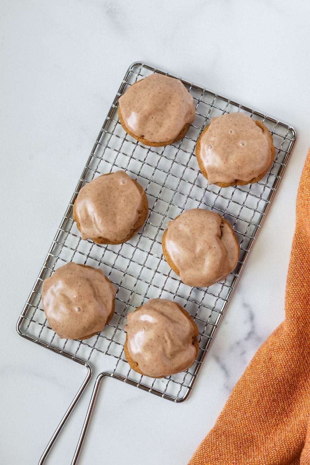 overhead view of six iced pumpkin spice cookies made with spice cake mix, displayed on a wire rack.