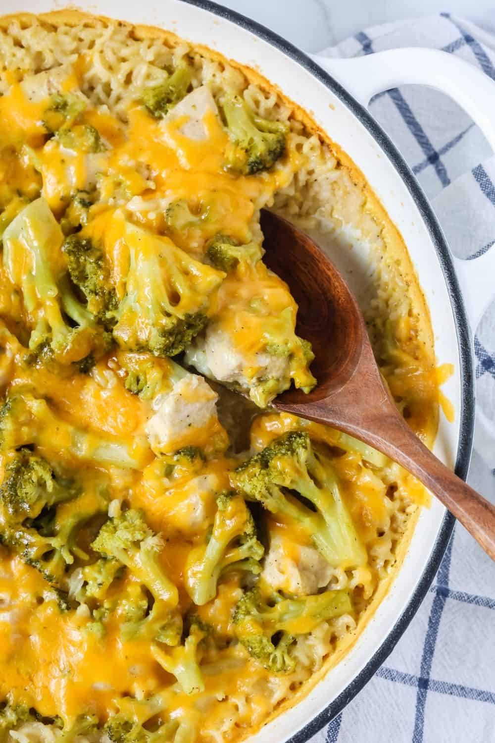 overhead view of a dutch oven braising pan filled with freshly baked chicken and rice casserole with broccoli and cheese. A wooden spoon is scooping out a serving.