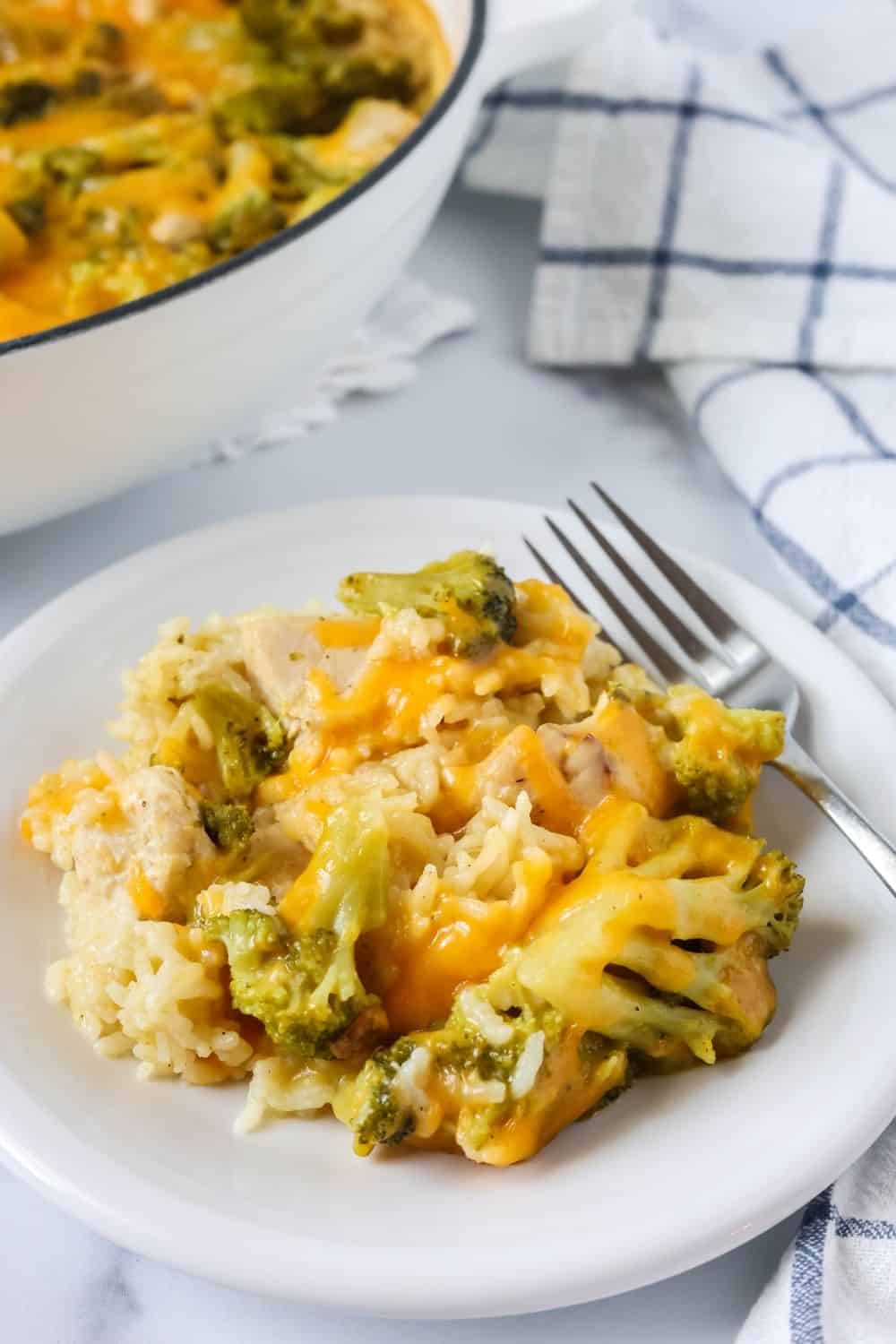 a white plate serves a helping of creamy chicken and rice with broccoli. A fork is on the plate, and the casserole pan is in the background.