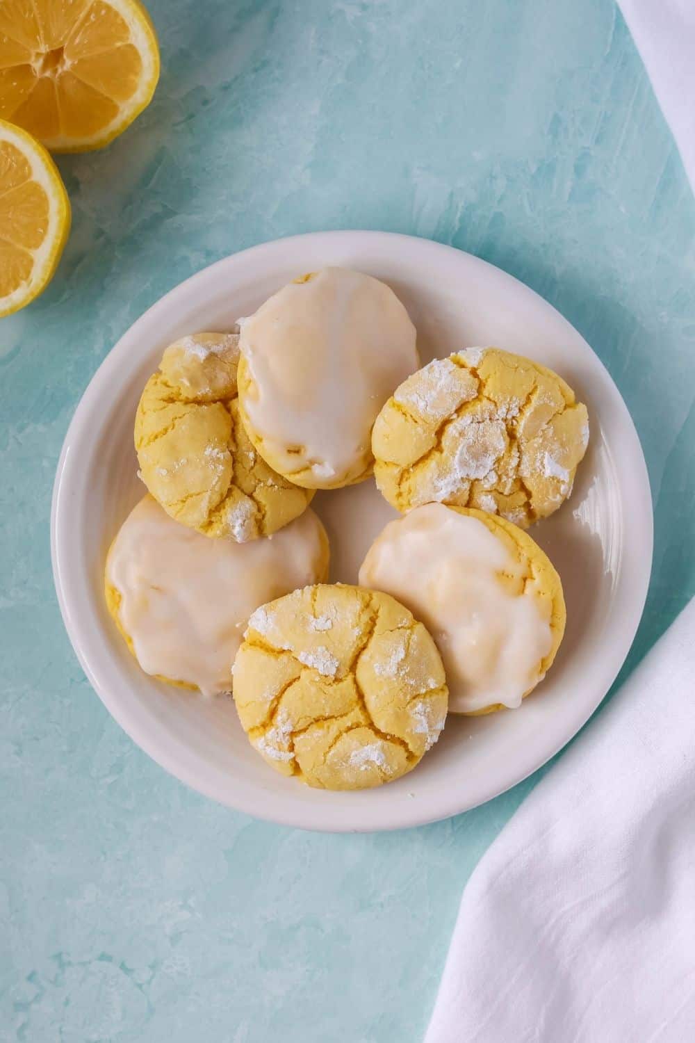 overhead view of a plate of lemon cake mix cookies; three are topped with lemon icing and three are lemon crinkle cookies.
