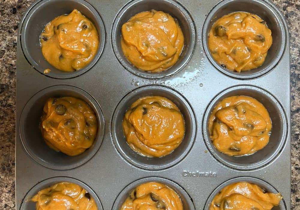 a muffin tin with the wells filled with pumpkin chocolate chip muffin batter.