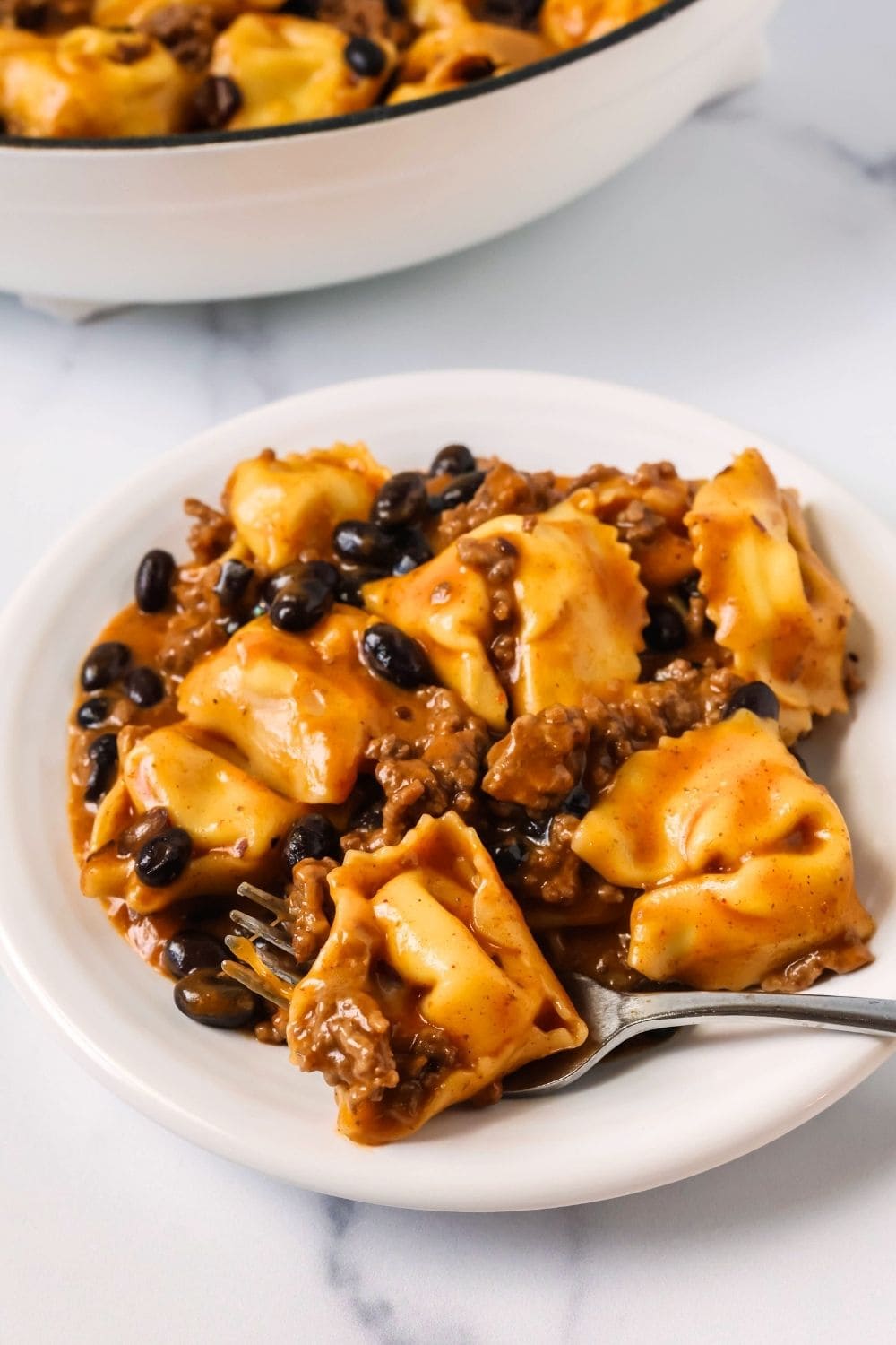 close-up view of a plate of beef enchilada tortellini, with a fork holding a piece of the tortellini.