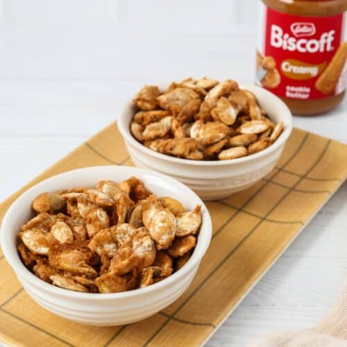 Biscoff cookie butter pumpkin seeds served in white bowls, with a jar of Biscoff in the background.