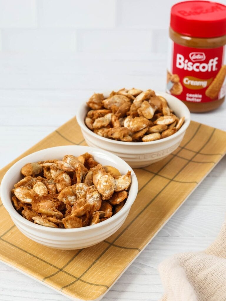 Biscoff cookie butter pumpkin seeds served in white bowls, with a jar of Biscoff in the background.