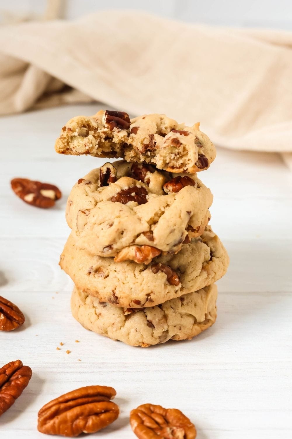 a stack of four cake mix pecan cookies. The cookie on top has a bite taken out of it, and pecan halves are scattered around the stack.