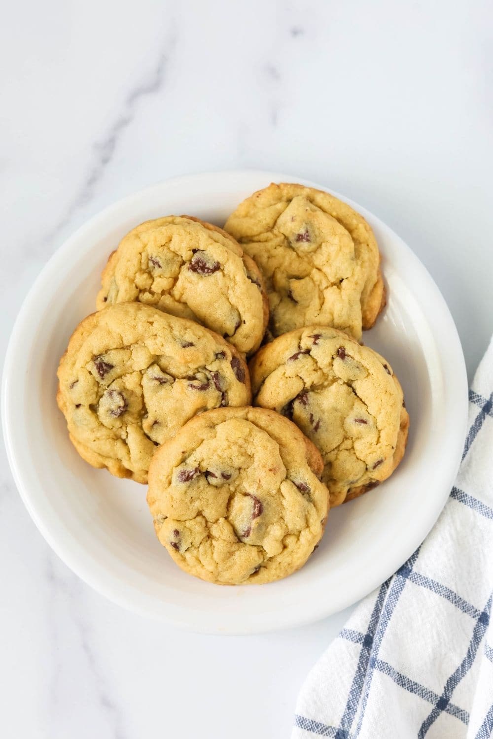 overhead view of five chocolate chip pudding cookies on a white plate, showing their golden-brown edges and thick texture.