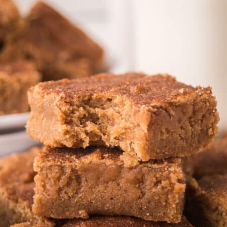 A few churro bars stacked together, one of which has a bite taken out of it, showing the soft and chewy texture.