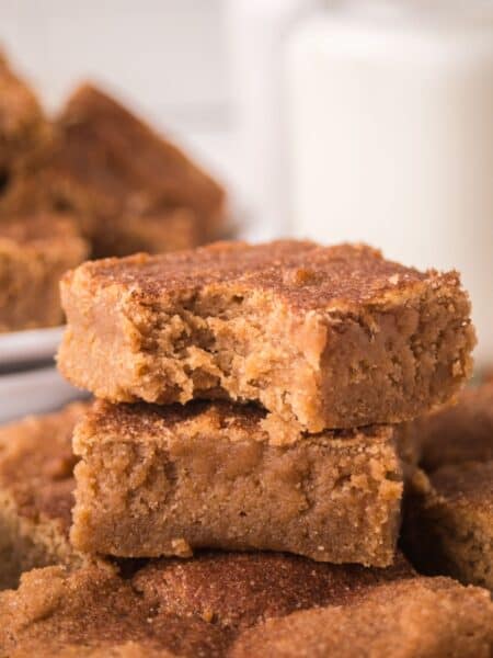A few churro bars stacked together, one of which has a bite taken out of it, showing the soft and chewy texture.