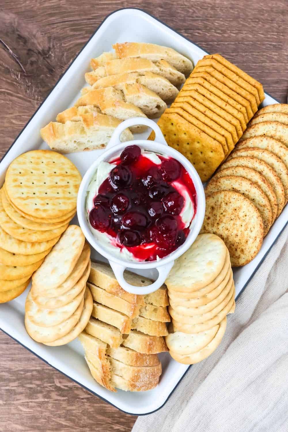 A platter serves cranberry Boursin cheese dip alongside an assortment of crackers and bread slices.