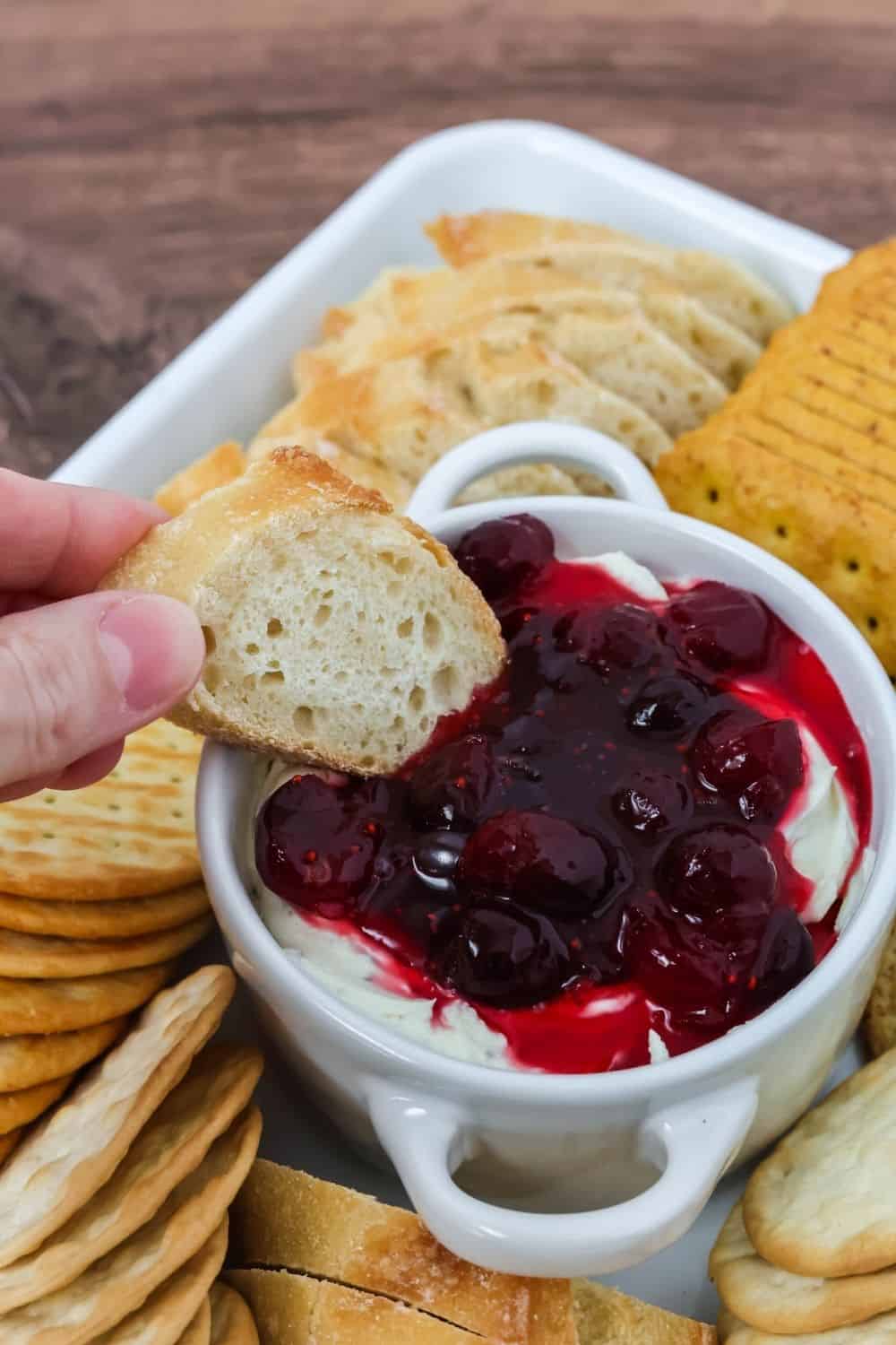 a hand dips a baguette slice into boursin and cranberry dip.