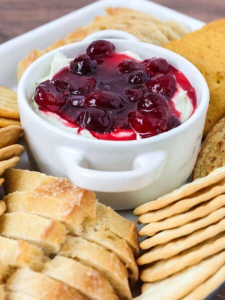Cranberry Boursin dip served in a small dish, surrounded by crackers and sliced baguette pieces.